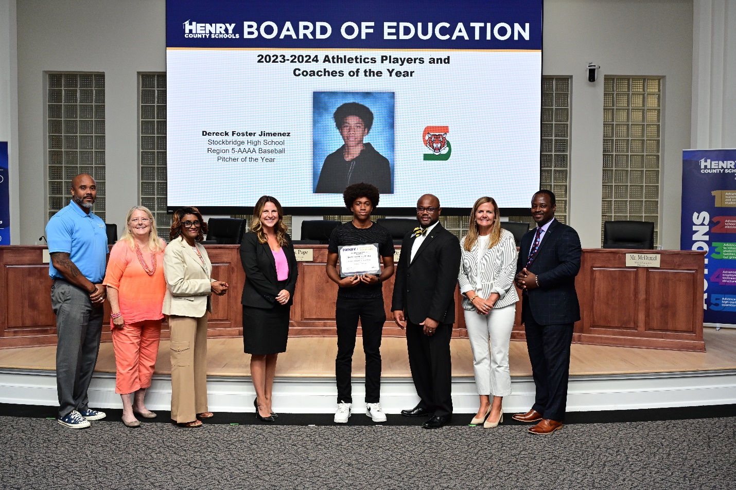 A group of people standing in front of a large screenDescription automatically generated